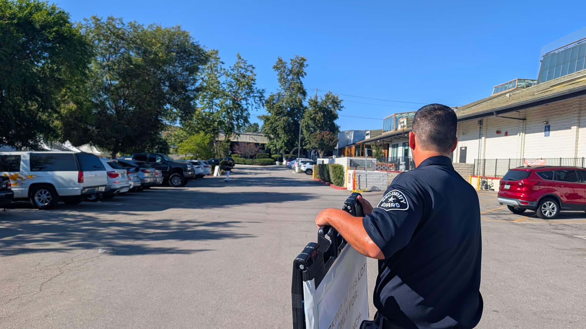 A uniformed security guard on duty in a commercial property parking lot on a sunny day